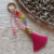 Pingente/chaveiro de bolsa, mosquetão e argola banhados a ouro. Entremeios banhados a ouro e ABS cor ouro velho. Contas de acrílico rosa e coloridas translúcidas. Conta de ABS cor arco-íris. Tassel de seda rosa. Peso: 19 g. Tamanho: 17 cm.