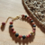 Pulseira boho de mola dourada. Pedras vulcânica preta e jaspe red. Entremeios folhados a ouro. Fecho lagosta. Extensor. Peso: 20 g. Tamanho: 6,5 cm de diâmetro.