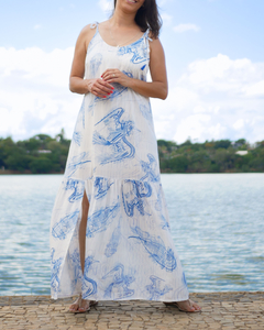 Vestido longuete Alegria, estampado em azul e branco, inspirado nos painéis de Cândido Portinari na igrejinha da Pampulha. O modelo é soltinho e leve. É confeccionado em viscose, possui forro, alças de amarrar, babado e fenda na barra.