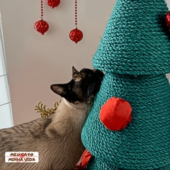 Gato interagindo com uma árvore de Natal arranhador, decorada com bolas vermelhas.