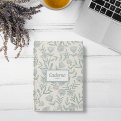 Caderno copta com estampa de flores da coleção Dandelion, posicionado sobre uma mesa com chá e um laptop.