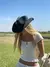 Mujer con un sombrero negro y una remera de rayas, sonriendo en un campo verde bajo un cielo despejado.