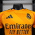 Camiseta de goleiro do Real Madrid na cor laranja, com o logo do time e patrocinador em destaque. camisa-camisas-blusa-blusas-uniforme-real-madrid-ii-2-segunda-segundo-24-25-jogador-adidas-masculina-masculino-laranja-vini-jr-mbappe-bellingham