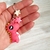 Chaveiro infantil em formato de dinossauro rosa com estrelas coloridas, segurado na mão.