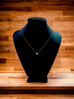 Collar dorado con un colgante brillante, exhibido en un maniquí negro sobre una superficie de madera.