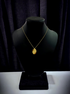 Collar dorado con colgante circular, exhibido en un maniquí sobre un fondo oscuro.