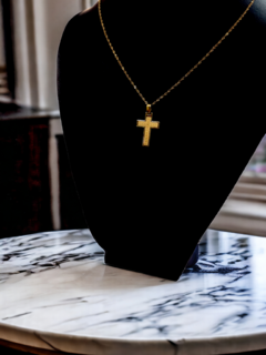 Cruz de oro de 18 quilates grande, arenada con detalles, exhibida en un soporte negro sobre una mesa de mármol.