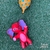 Um elefante vermelho com orelha roxa olhos azuis e barriguinha rosa segurando um balão amarelo com pontinhos azuis