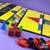 Tabuleiros de jogos amarelos com peças coloridas em vermelho, amarelo, azul e verde, dados vermelhos com detalhes pretos e peças redondas em vermelho e preto