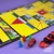 Tabuleiros de jogos amarelos com peças coloridas em vermelho, amarelo, azul e verde, dados vermelhos com detalhes pretos e peças redondas em vermelho e preto