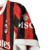 Nova camisa titular do AC Milan 24/25: listras vermelhas e pretas em tom sobre tom, gola e punhos brancos. Escudo e logo PUMA em branco. Costas vermelhas com selo dos 125 anos.