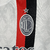 Camisa reserva do Milan 23/24 é branca com duas listras verticais em vermelho e preto. Detalhes em prata por toda camisa. Escudo e logos puma prateados.