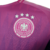 A nova camisa reserva da Alemanha apresenta degradê em rosa e roxo, inspirado na águia, com detalhes rosados na gola, ombros e recortes curvos. Logos Adidas e DFB em rosa.