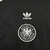 Camisa de viagem da Alemanha Adidas 2024: Preto predominante. Mangas brancas com detalhes em preto, vermelho e amarelo remetendo à bandeira alemã. Escudo Alemanha e logo Adidas trefoil centralizados, trazendo o aspeto retrô.