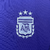 O manto feminino reserva da Argentina 2024 destaca o azul royal, homenageando Maradona. As listras celestes nos ombros representam a bandeira. Logos Adidas e AFA em celeste, com o patch de campeã mundial no peito.