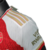 Camisa titular do Arsenal 23/24 versão jogador: vermelha com mangas brancas. Raios dourados, faixas com "W" e "D" (invencibilidade 2003-2004). Escudo Arsenal e logo Adidas bordados.