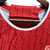 Camisa manga longa titular do Arsenal 23/24: vermelha com mangas brancas. Raios dourados, faixas com "W" e "D" (invencibilidade 2003-2004). Escudo Arsenal e logo Adidas bordados.