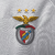 Terceira camisa branca do Benfica com detalhes vermelhos, inspirados nos cinco continentes. Escudo, logo Adidas e patrocínios em preto. Selo de 120 anos na nuca.