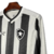 Visão lateral da camisa titular 2024 manga longa do Botafogo. Tem listras verticais com textura em zigue-zague. Gola V branca com bordas pretas e mangas listradas. Escudo alvinegro e logo Reebok em TPU.