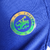 Camisa titular feminina Chelsea: Azul com detalhes em branco, homenageando kit de 1997/98. Escudo e logo Nike em dourado iridescente. Gola redonda azul, punhos brancos com detalhes azul marinho e dourado.