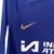 Camisa manga longa titular Chelsea 23/24: Azul com detalhes em branco, homenageando kit de 1997/98. Escudo e logo Nike em dourado iridescente. Gola redonda azul, punhos brancos com detalhes azul marinho e dourado.