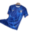 Camisa titular do Chelsea 24/25 é azul royal com padrão de ondas claras, simbolizando chamas. Gola redonda azul, punhos brancos e laranja. Escudo e logo Nike em azul celeste com contorno laranja.