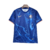 Camisa titular do Chelsea 24/25 é azul royal com padrão de ondas claras, simbolizando chamas. Gola redonda azul, punhos brancos e laranja. Escudo e logo Nike em azul celeste com contorno laranja.