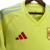 Camisa reserva da seleção espanhola 2024 amarela neon inspirada no sol e verão espanhol. Laterais com ondas azul celeste, arcos vermelhos, três listras nas mangas e faixa na gola. Escudo RFEF amarelo e vermelho no peito esquerdo, logo Adidas no direito.