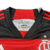 Peitoral da camisa feminina titular 2024 Flamengo vista de frente: Gola V preta com detalhes em vermelho e prata. Escudo CRF e logo Adidas bordados em prata.