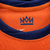 A nova camisa da Holanda celebra a cultura holandesa com um tom de laranja atualizado. A gola redonda, punhos e laterais são azul escuro com detalhes azul celeste. O escudo e o logo da Nike são azul escuro.