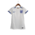 Camisa titular da seleção inglesa feminina com detalhes em azul inspirada em tijolos brancos de Wembley em 1923 e na seleção feminina inglesa de 1984. Escudo da Federação Inglesa à esquerda, logo Nike azul à direita.