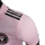 Camisa titular rosa do Inter Miami, chamada "Heartbeat Kit", com gola polo e listras pretas nos ombros. Mangas rosa com punhos com batimentos cardíacos em relevo. Escudo Inter Miami e logo Adidas e em preto.