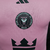 A camisa titular 24/25 rosa do Inter Miami, 'Easy Pink', traz faixas e detalhes pretos, com escudo, logo da Adidas e Royal Caribbean em preto. A frase 'Liberdade para Sonhar' na nuca e barra complementa o design.