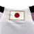 Camisa reserva do Japão 2022: branca com origamis azuis e vermelhos nas mangas. Gola V em azul marinho, escudo da Federação à esquerda, logo Adidas em azul marinho à direita. 