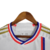 Camisa titular Lyon: branco predominante, faixa vertical vermelha e azul royal no lado esquerdo. Gola V tricolor, três listras douradas nas mangas. Logo Adidas dourado no peito direito, escudo Lyon à esquerda. Manto representa herança e cultura.