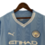 Camisa manga longa titular Manchester City 23/24: azul celeste com faixas verticais em tom sobre tom, inspiradas nas torres do Etihad Stadium. Gola V branca com frisos azul celeste. Escudo do clube e logo puma bordados.