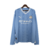 Camisa manga longa titular Manchester City 23/24: azul celeste com faixas verticais em tom sobre tom, inspiradas nas torres do Etihad Stadium. Gola V branca com frisos azul celeste. Escudo do clube e logo puma bordados.