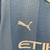 Camisa manga longa titular Manchester City 23/24: azul celeste com faixas verticais em tom sobre tom, inspiradas nas torres do Etihad Stadium. Gola V branca com frisos azul celeste. Escudo do clube e logo puma bordados.