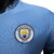 A camisa titular do Manchester City 24/25 versão jogador mantém o azul celeste predominante, com faixas diagonais azul marinho. Detalhes celestes nos punhos e gola, com o código "0161". Logos PUMA em branco.