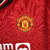 Camisa titular feminina do Manchester United: vermelha com padrão gráfico de rosas, gola preta com detalhes em branco e vermelho, escudo do United à esquerda, logo Adidas em branco à direita.