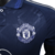 A nova camisa reserva do Manchester United 24/25 versão jogador traz base azul escuro com padrão de "M" formando estrelas. Detalhes em azul e três listras em prata nos ombros. Escudo e logo Adidas em prata.