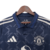 A nova camisa reserva do Manchester United 24/25 traz base azul escuro com padrão de "M" formando estrelas. Detalhes em azul e três listras em prata nos ombros. Escudo e logo Adidas em prata.