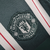 Camisa reserva Manchester United 23/24: Verde escuro com faixas verticais brancas e linhas vermelhas. Gola branca, três listras nos ombros em branco. Escudo Man United verde e branco, logo Adidas branco.