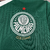 Camisa titular feminina Palmeiras 2024: design clássico, verde predominante, gola pólo e punhos brancos. Três emblemas históricos celebram 110 anos do clube. PUMA estampa felino e patrocinador em dourado, escudo atual no lado esquerdo.