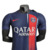 Nova camisa titular do PSG: azul marinho com faixa vertical deslocada, degradê branco. Gola redonda azul, escudo na faixa, logo Nike vermelho. Bandeira da França nas costas. 