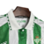 Camisa titular do Real Bétis 2024-2025: listras verticais verde e branco, padrão brilhante inspirado nos anos 90. Gola polo branca com detalhes serrilhados em verde, logo Hummel em branco e chevrons nos ombros.