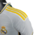 Camisa titular Real Madrid branca com gola em V e frisos em azul marinho, branco e dourado. Escudo no peito e logo Adidas em azul marinho. Frase "¡Hala Madrid!" na nuca.