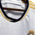 Camisa titular manga longa Real Madrid branca com gola em V e frisos em azul marinho, branco e dourado. Escudo no peito e logo Adidas em azul marinho. Frase "¡Hala Madrid!" na nuca.