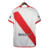 Camisa branca do River Plate com faixa diagonal vermelha. Detalhes em vermelho na gola V, três listras, punhos, laterais e barra. Escudo Millonarios na faixa à esquerda, logo Adidas vermelho à direita. 'Grandeza' na nuca .