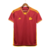 Camisa titular AS Roma 23/24: Vermelha com detalhes amarelos na gola, punhos, laterais e listras dos ombros. Escudo Lupetto histórico, logo Adidas amarelo no peito, frase "Daje Roma Daje" na nuca.